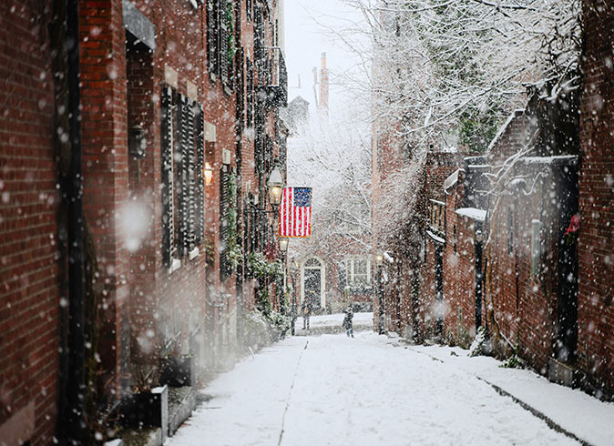 A snow covered street with brick buildings on both sides and an American flag