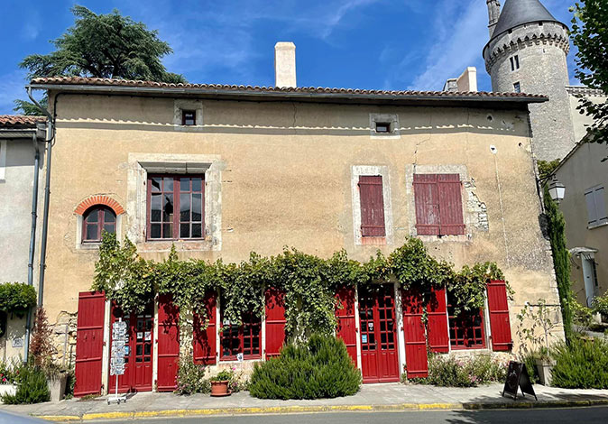 A brown, stone, typical French countryside building with red doors and shutters