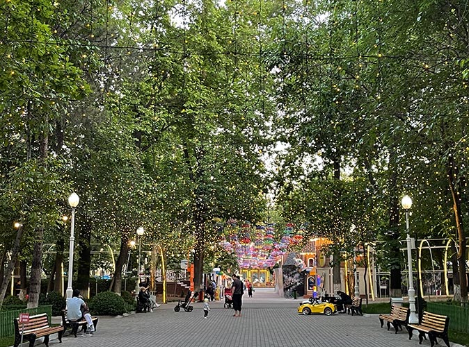 A park in Tashkent with large green trees and several people walking on a paved path