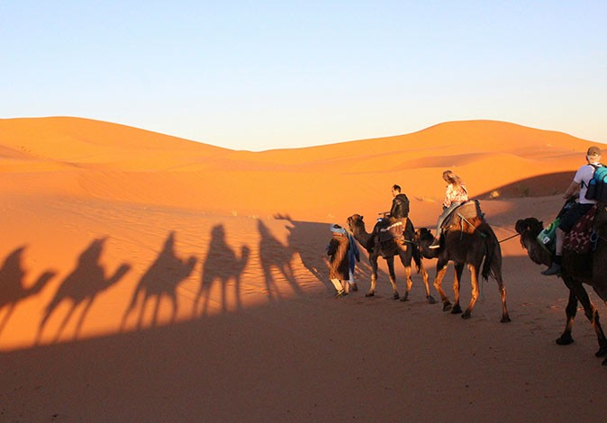 3 people being guided on camels in a desert