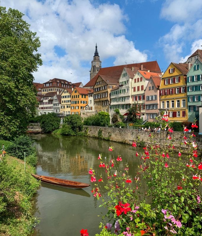 A picture of the iconic Neckarbrcke in Tubingen. You can see a Stocherkhne resting in the water, the colorful buidlings in the background, and all kinds of blossoming flowers in the front. Seeing this gorgeous view of Tubingen is a must things to do in the city.