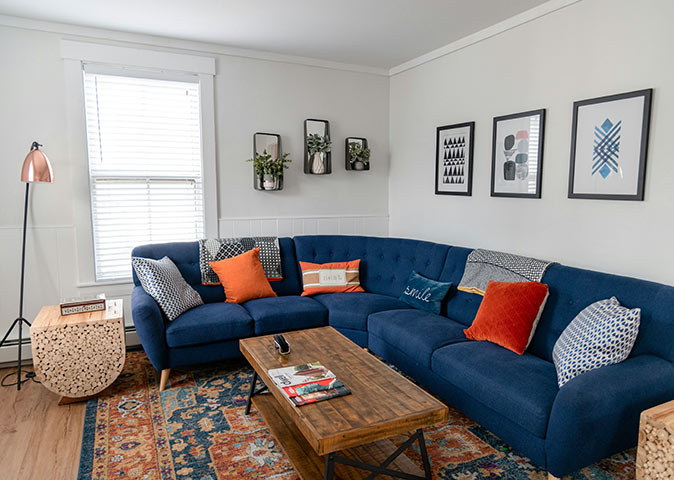 living room with a large dark blue couch, white walls, a wooden table and several small items