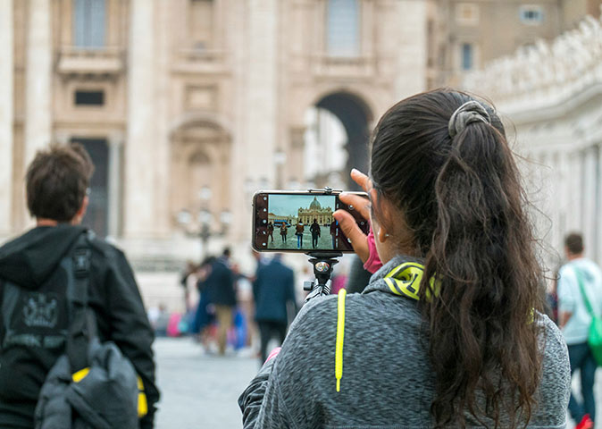 A woman holding a phone, taking a picture of the Vatican
