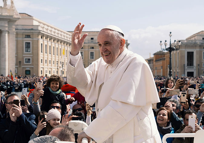 Pope Francis waving at the Vatican, surrounded by a lot of people