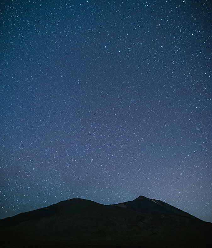silhouette of a mountain with a dark blue sky filled with stars