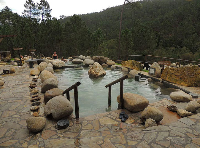 an outdoor thermal bath surrounded by brown rocks and green hills