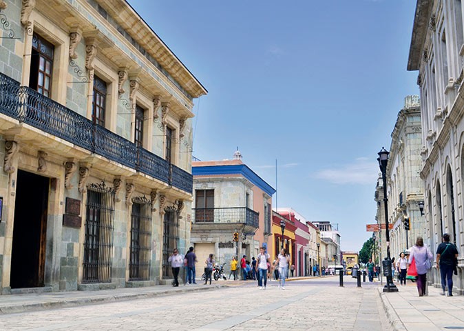 A wide street with several people, lined with typical Mexican buildings