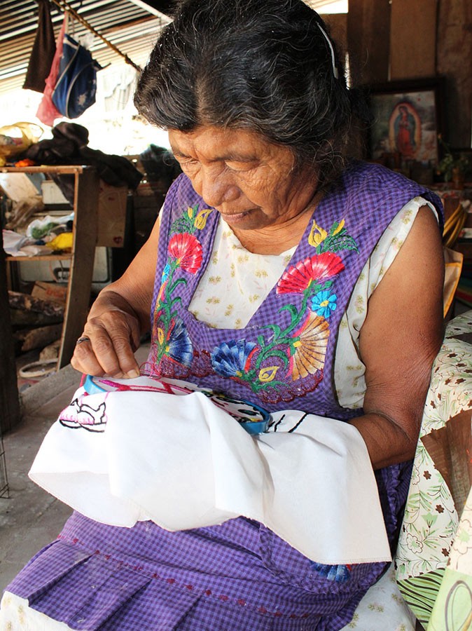 A Mexican woman in a purple dress doing traditional embroidery
