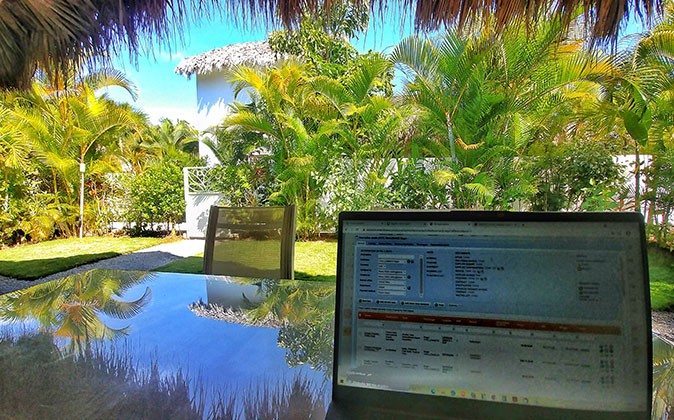 a laptop on a glass table looking out towards a yard with lush greenery