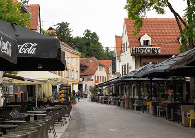 A pedestrianized street lined with restaurants with tables, chairs and umbrellas outside
