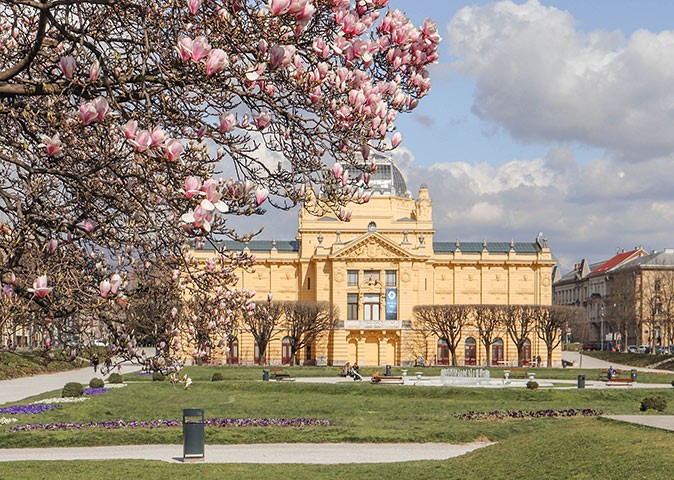 A grand, historic yellow building with a park and a blossom tree in front of it