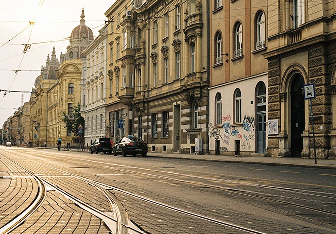 tramway tracks on a wide road with 2 parked cars and historic buildings on one side