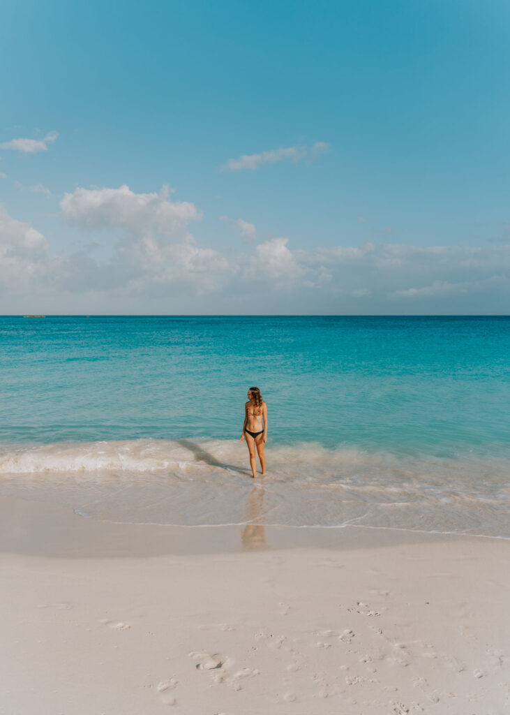 Woman standing beside small waves on a white sandy beach in the Bahamas