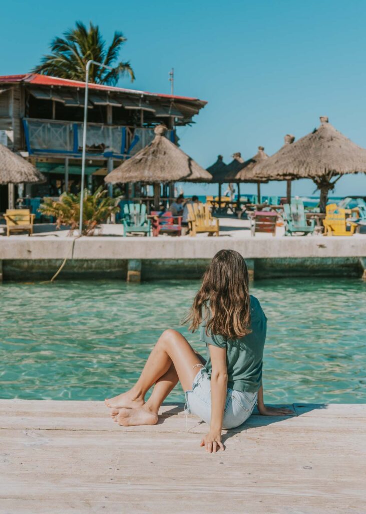 Woman sitting on dock at the Split in Caye Caulker, Belize thinking of the best island Instagram captions