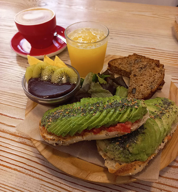 A vegan brunch consisting of coffee, juice, acai, cake and bread with avocado and tomato