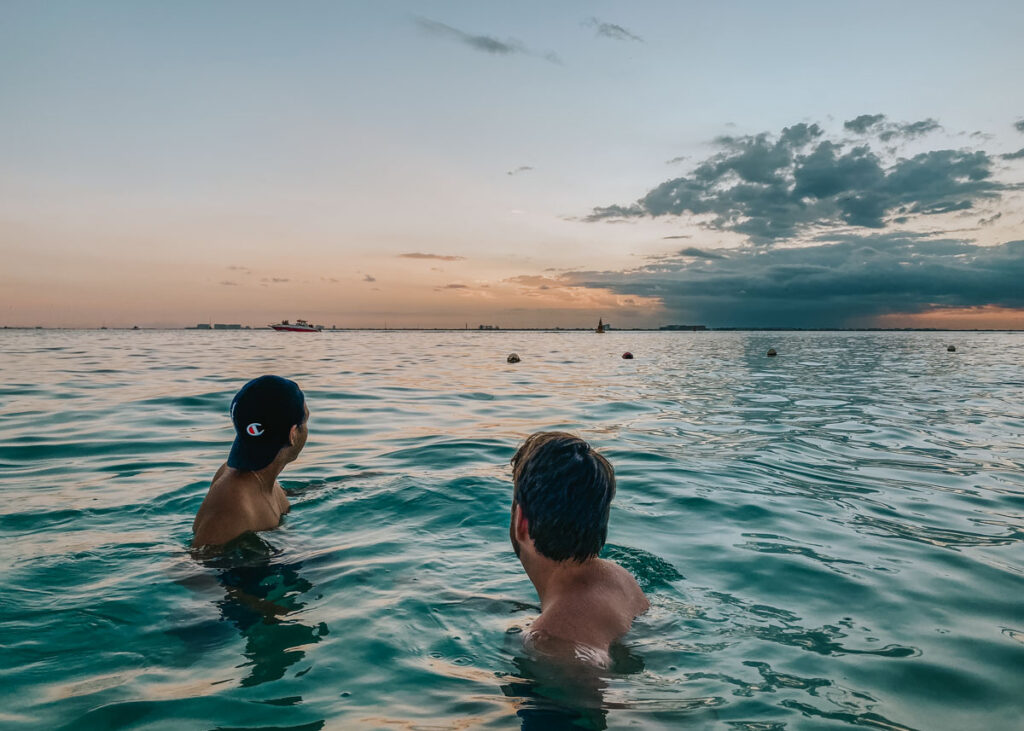 Two men in the water watching the sunset from Isla Mujeres