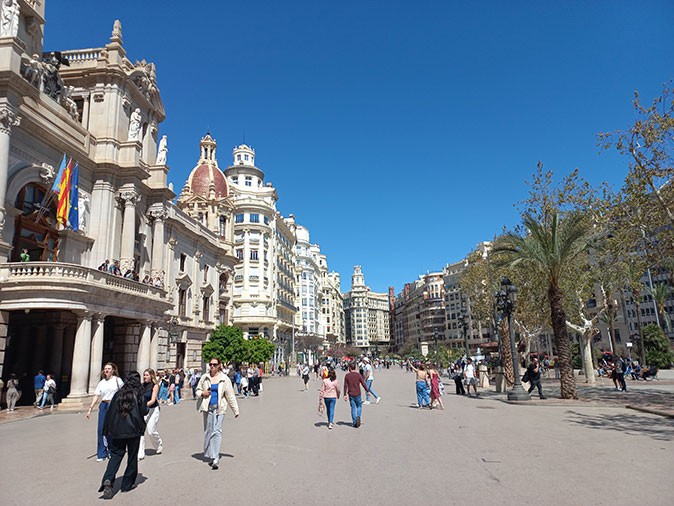 A large city square with many pedestrians, trees, and historic buildings