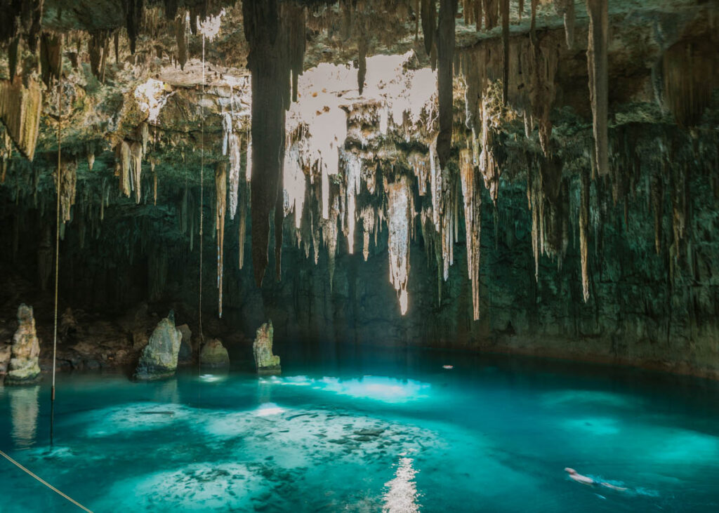 Expansive Xcanahaltun cenote with turquoise water, and stalactites hanging from the cave ceiling